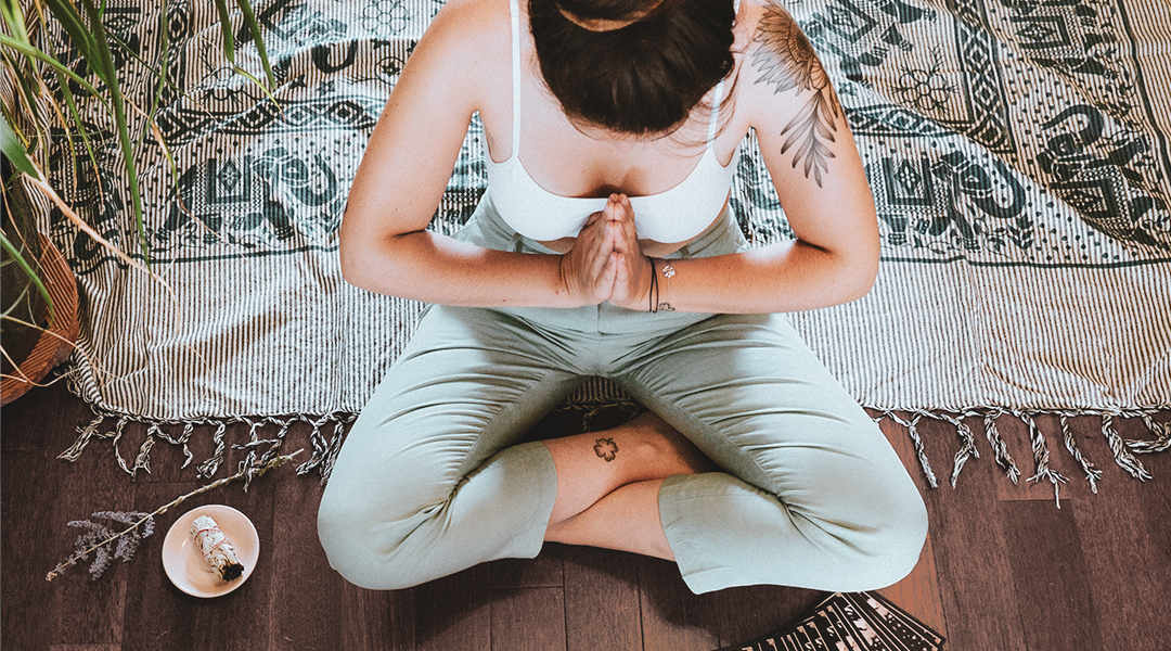 Femme assise en tailleur, les mains joints devant son cœur.