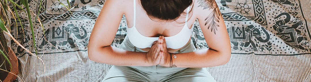 Femme assise en tailleur, les mains joints devant son cœur.