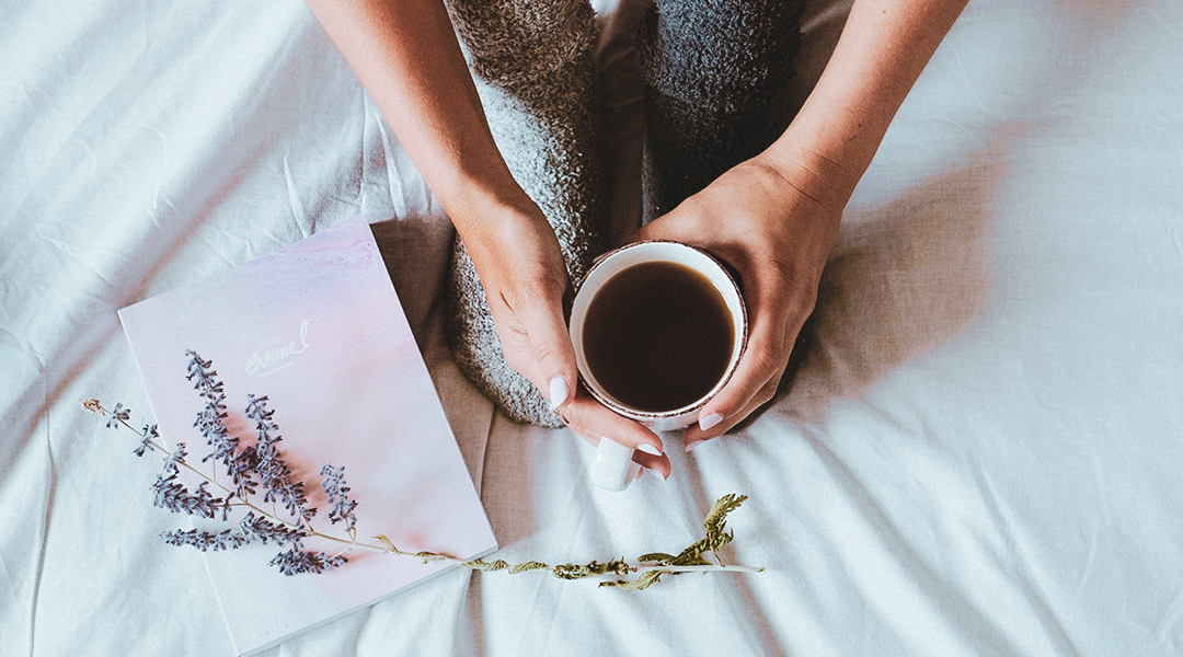 Tasse de thé tenue sur un lit au côté d'un agenda evonel et une branche de lavande.